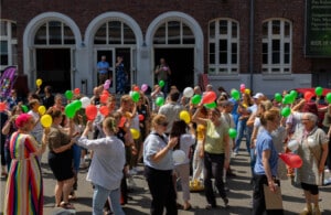 Eine große Personengruppe geht mit bunten Luftballons kreuz und quer über einen Platz